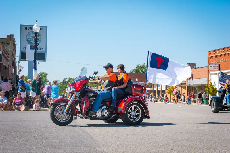 Riders on a red motorcycle trike carry a Christian flag down the parade route.