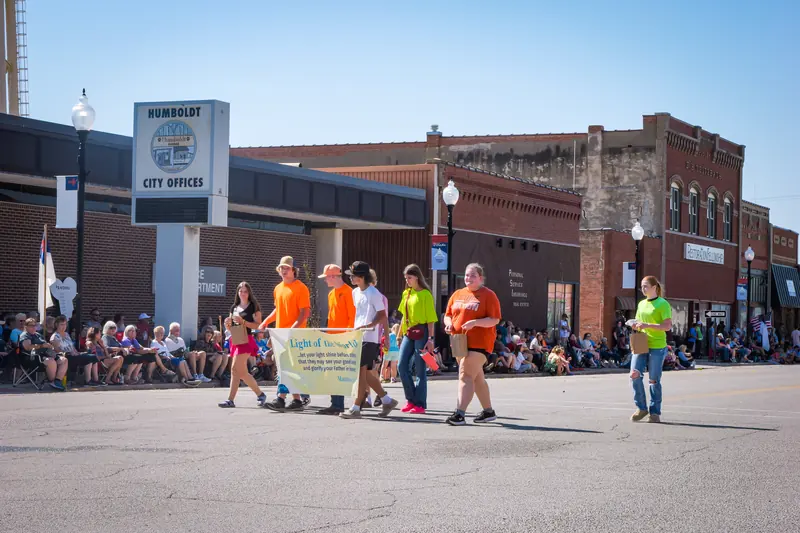 Young people in bright T-shirts carry a banner past spectators seated along the curb.