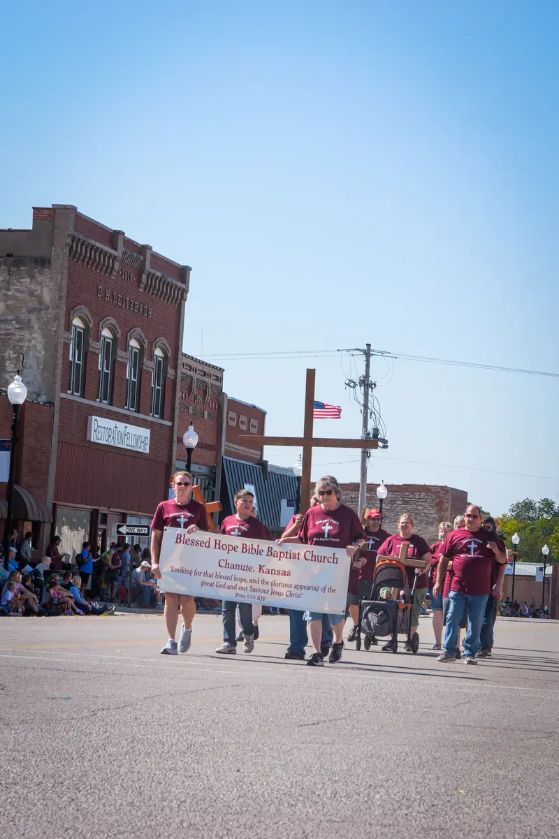 A church group walks behind its banner, with a wooden cross raised above them.