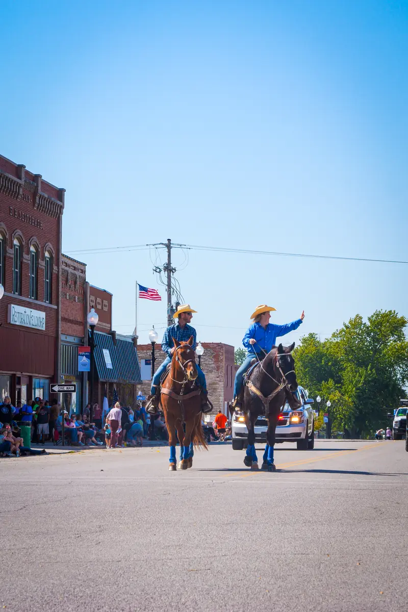 Two riders on horseback wave to the crowd along the parade route.