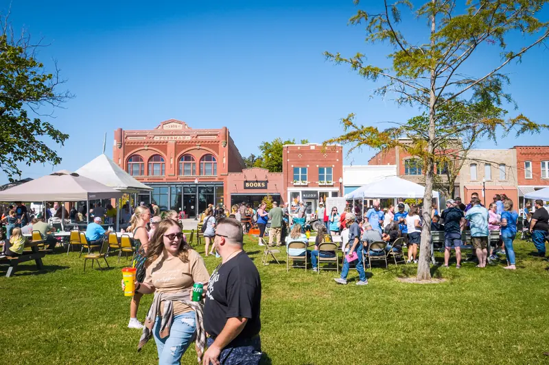 Visitors stroll between tents and picnic tables on the Town Square, with historic brick storefronts behind.