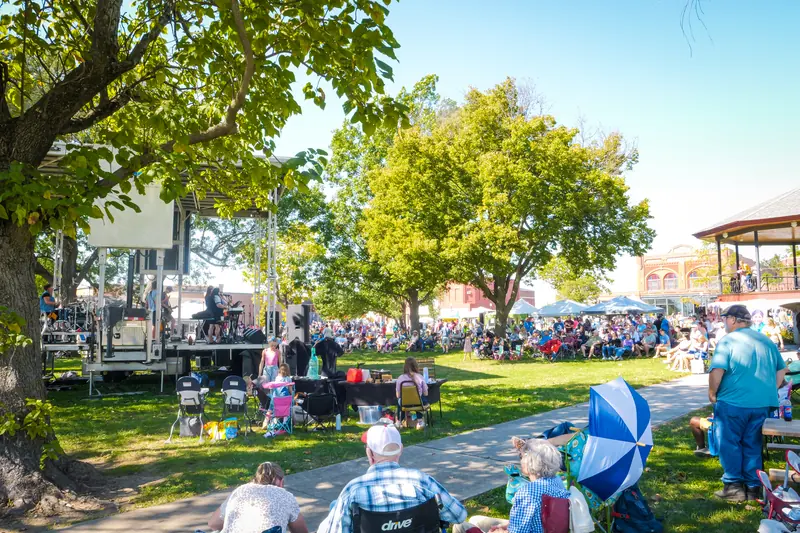 Families on lawn chairs and blankets listen to music under the trees on the Town Square.
